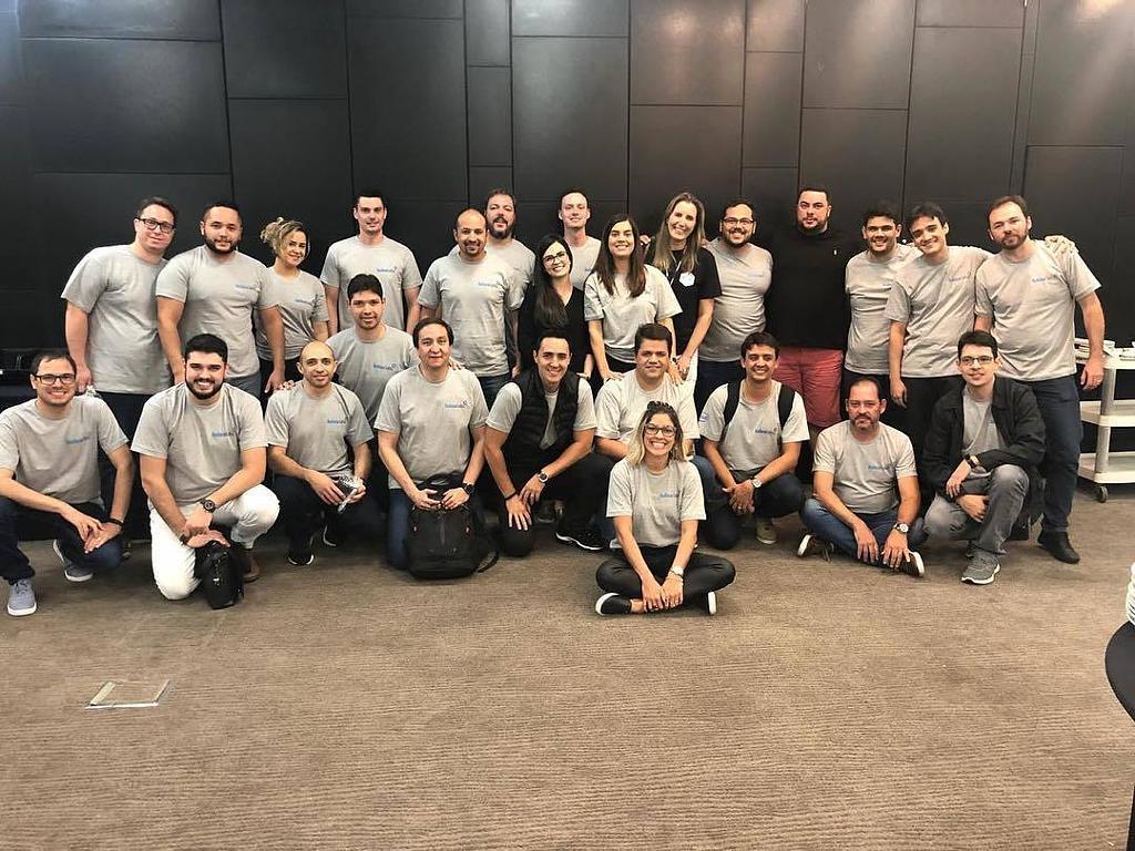Time de tecnologia reunido em sala corporativa, todos com camisetas do laboratório de inovação.