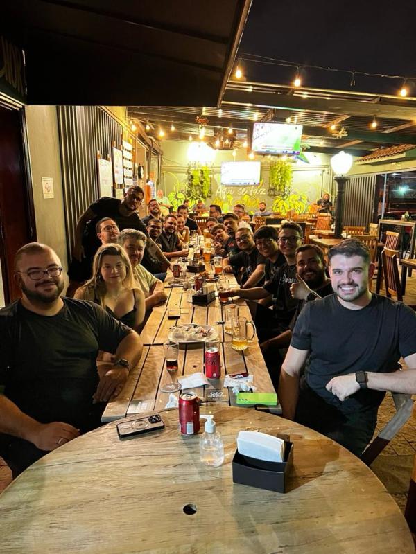 Time de tecnologia do Grupo Multi reunido em confraternização em volta de uma mesa longa em um bar.